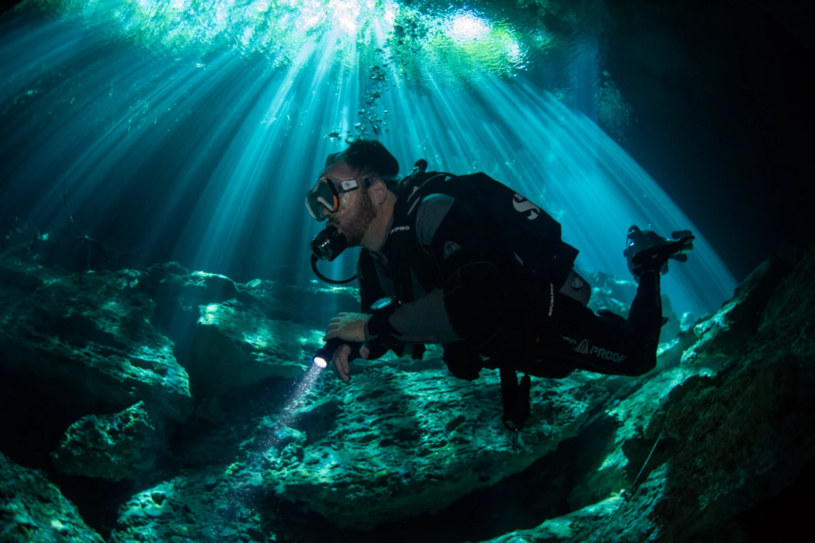 Advanced Open Water diver with a torch under shafts of light in a cenote
