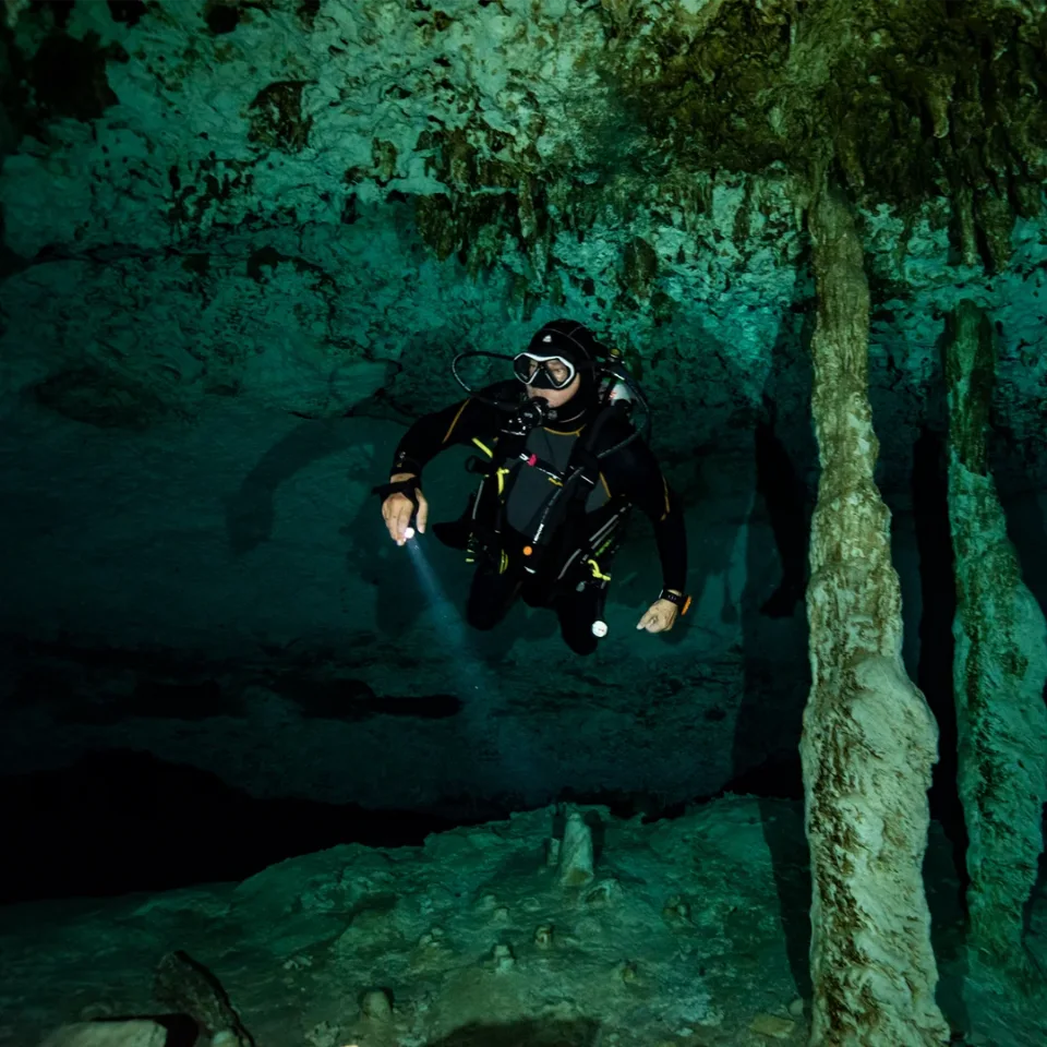 Diver with a torch beside a stalactite column at Cenote Dos Ojos