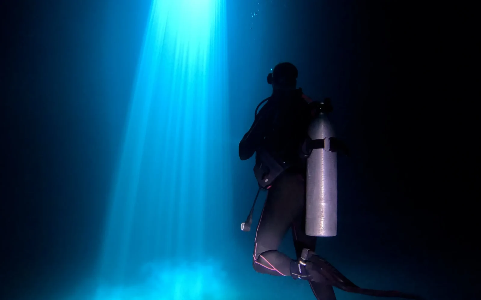 Diver silhouetted beside a beam of light in a Puerto Morelos cenote